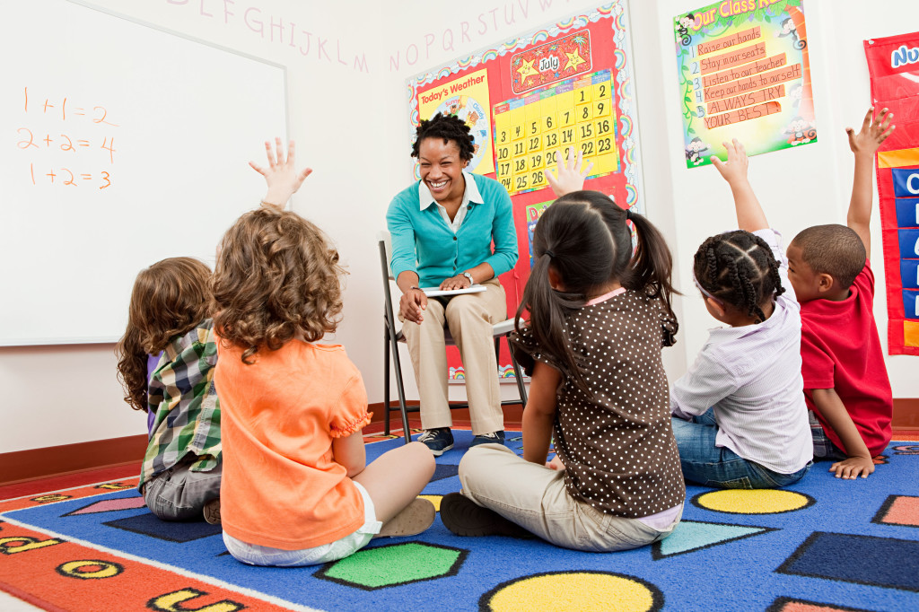 Teacher and children sitting on floors with hands raised